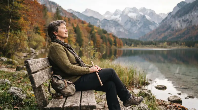 Eine Frau um die fünfzig ruht auf einer Bank am Ufer eines Bergsees.
